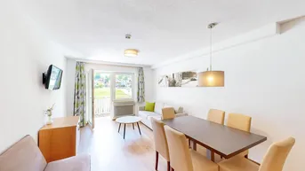 Helles Wohn- und Esszimmer mit Holzboden, Balkonzugang und Blick ins Grüne.