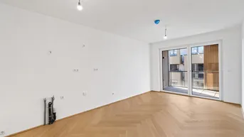 Helles, leeres Wohnzimmer mit Fischgrätparkett und Zugang zu einem Balkon.