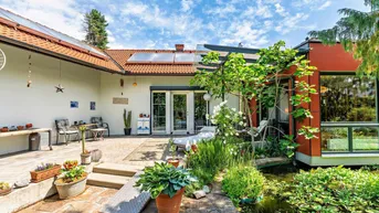 Sonnige Terrasse mit Sitzgelegenheiten, umgeben von einem gepflegten Garten und einem Teich.