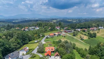 Luftaufnahme einer hügeligen Landschaft mit Wohnhäusern, Straßen und weiten Waldgebieten.
