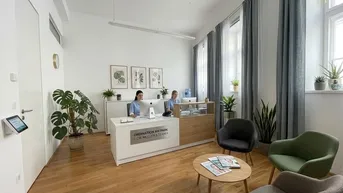 Heller Empfangsbereich mit Holzboden, modernen Möbeln und großen Fenstern, die viel Tageslicht hereinlassen.