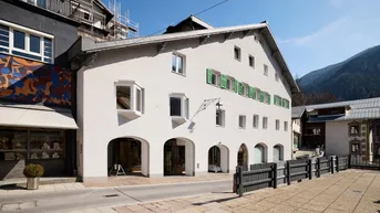 Historisches Gebäude mit weißer Fassade, grünen Fensterläden und Bergblick in einer malerischen Gasse.