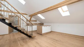 Heller offener Wohnbereich im Dachgeschoss mit moderner Küche, Holzbalken und schmiedeeiserner Treppe.