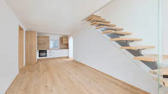 Heller offener Wohnbereich mit moderner Einbauküche, Holzfußboden und eleganter Holztreppe mit Glasgeländer.