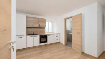 Helle Küche mit Holz- und weißen Fronten, ausgestattet mit modernen Geräten und Blick ins Badezimmer.