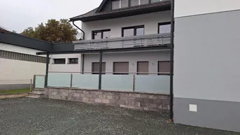 Modernes Gebäude mit Balkon, Glasgeländer und Kiesfläche im Vordergrund.