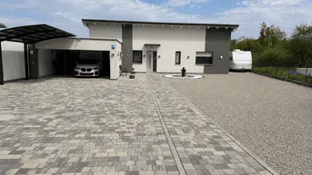 Modernes Einfamilienhaus mit gepflasterter Auffahrt, Carport und Zierbrunnen im Vorgarten.