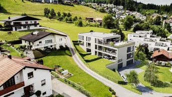 Luftaufnahme eines modernen Wohngebäudes in einer grünen, hügeligen Wohngegend.