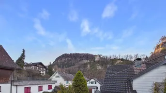 Panoramablick auf eine bergige Landschaft mit Häusern und einem blauen Himmel.