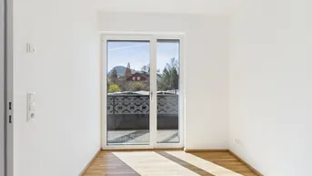 Helles Zimmer mit Parkettboden und Zugang zu einem Balkon, der einen Blick auf die Umgebung bietet.