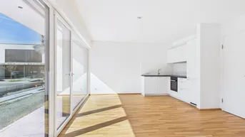 Offener Wohnbereich mit integrierter Küchenzeile, Parkettboden und großen Fenstern zur Straße.