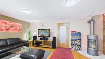 Gemütliches Wohnzimmer mit Kaminofen, Holzboden und schwarzem Ledersofa.