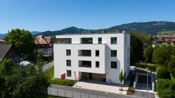 Moderne Wohnanlage mit weißer Fassade und Bergblick in grüner Umgebung.