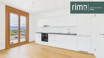 Helle, moderne Küche mit weißen Hochglanzfronten, Holzboden und Zugang zum Balkon mit Weitblick.
