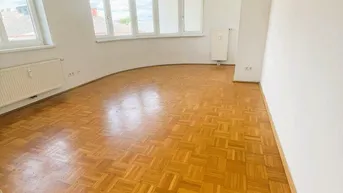 Helles Wohnzimmer mit Parkettboden und einem markanten Erkerfenster, das viel Tageslicht hereinlässt.