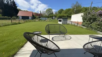 Moderne Terrasse mit Sitzgelegenheiten und Blick auf den grünen Garten an einem sonnigen Tag.