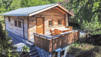 Helles Holzchalet mit großer Terrasse und Esstisch im Grünen, umgeben von Natur.