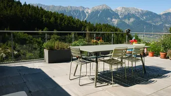 Große Terrasse mit Esstisch und Stühlen, umgeben von grünen Bäumen und einem beeindruckenden Bergblick.