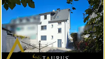 Modernes weißes Mehrfamilienhaus mit grauen Fenstern und Dach, umgeben von Grün.