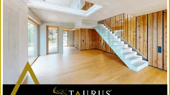 Geräumiger Wohnbereich mit Holzboden, Sichtbetonwänden und moderner Glas-Beton-Treppe.