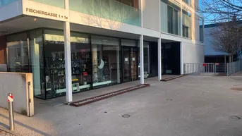 Modernes Gebäude mit großen Schaufenstern im Erdgeschoss und einer Rampe zum Eingangsbereich.