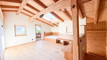 Helles Zimmer mit Holzbalkendecke, Dachfenster und Holzboden, ideal als Wohn- oder Schlafbereich.