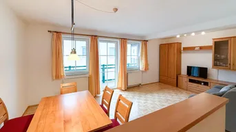 Heller Wohn- und Essbereich mit Holzmöbeln, Parkettboden und Zugang zum Balkon.