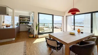 Heller offener Wohn- und Essbereich mit moderner Küche und direktem Zugang zur Terrasse mit See- und Bergblick.