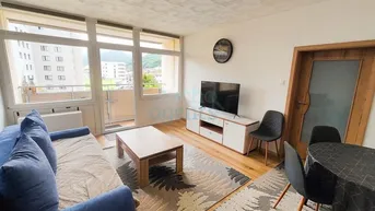 Helles Wohn- und Esszimmer mit modernem Sofa, Holzboden und Zugang zum Balkon mit Bergblick.