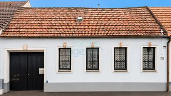 Traditionelles Haus mit weißer Fassade, schwarzen Fenstern und einem Satteldach mit Ziegeln.