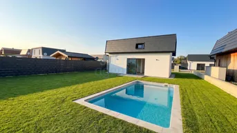 Neues Einfamilienhaus mit privatem Pool und gepflegtem Rasen unter blauem Himmel.