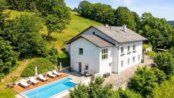 Idyllisches Anwesen mit weißem Haus, großem Pool und Sonnenterrasse inmitten grüner Hügellandschaft.
