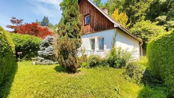 Charmantes Haus mit Holzfassade und gepflegtem Garten in grüner Umgebung.