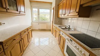 Funktionale Küche mit Holzschränken, Fliesenboden und Fensterblick.