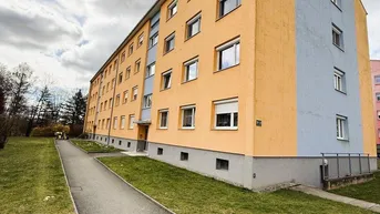 Mehrfamilienhaus mit orange-blauer Fassade und Grünflächen in der Umgebung.