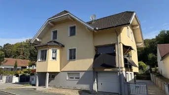 Gelbes Einfamilienhaus mit Satteldach, Garage im Untergeschoss und Balkon.
