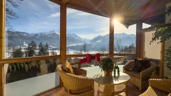 Heller Wintergarten mit Korbmöbeln und atemberaubendem Panoramablick auf die verschneiten Berge.