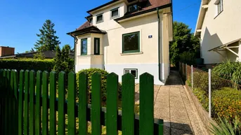 Traditionelles Haus mit heller Fassade, grünen Fensterrahmen und einem gepflegten Vorgarten.