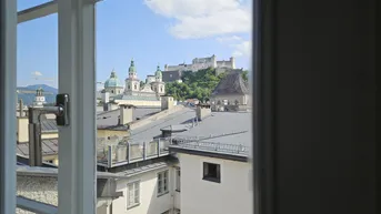 Blick aus dem Fenster auf die historische Stadt Salzburg mit Festung Hohensalzburg und Dächern.