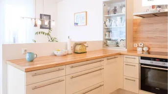 Moderne Küche mit hellen Holz-Arbeitsplatten, cremefarbenen Schränken und integrierten Geräten.