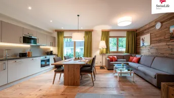 Helles, offenes Wohn-Esszimmer mit integrierter Küche, Holzboden und alpiner Wandverkleidung.