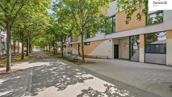 Moderne Wohngebäude-Fassade mit großen Fenstern und begrüntem Gehweg in einer ruhigen Wohngegend.