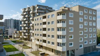 Moderne Wohngebäude mit mehreren Etagen, Balkonen und gepflegten Außenanlagen unter blauem Himmel.
