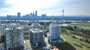 Luftaufnahme einer Baustelle mit mehreren im Bau befindlichen Gebäuden und Stadtpanorama im Hintergrund.