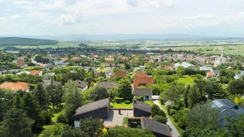 Weitläufige Luftaufnahme der Siedlung mit dem Anwesen im Vordergrund und hügeliger Landschaft.