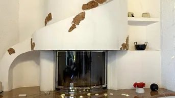 Moderner Kamin mit Glasfront und geschwungenen Formen, integriert in eine weiße Wand mit Fliesenboden.