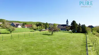 Weitläufige Grünfläche mit Obstbäumen und Blick auf die umliegende Landschaft und ein Dorf.