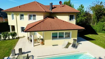 Großzügiges Einfamilienhaus mit Pool, Terrasse und weitläufigem Garten unter blauem Himmel.