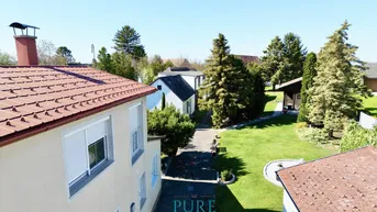 Luftaufnahme eines Hauses mit großem Garten und umliegenden Bäumen unter blauem Himmel.