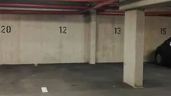 Tiefgarage mit nummerierten Stellplätzen, Betonwänden und sichtbaren Leitungen an der Decke.